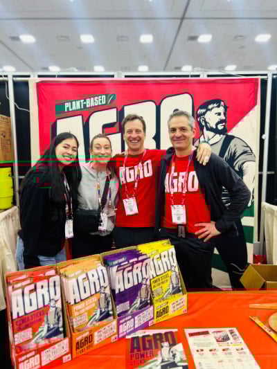 Two women and two men smiling in front of AGRO's Expo West booth.