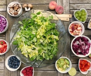 Table top set with a large bowl of salad greens with smaller bowls of fresh fruits and vegetables