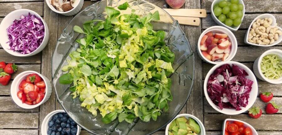 Table top set with a large bowl of salad greens with smaller bowls of fresh fruits and vegetables